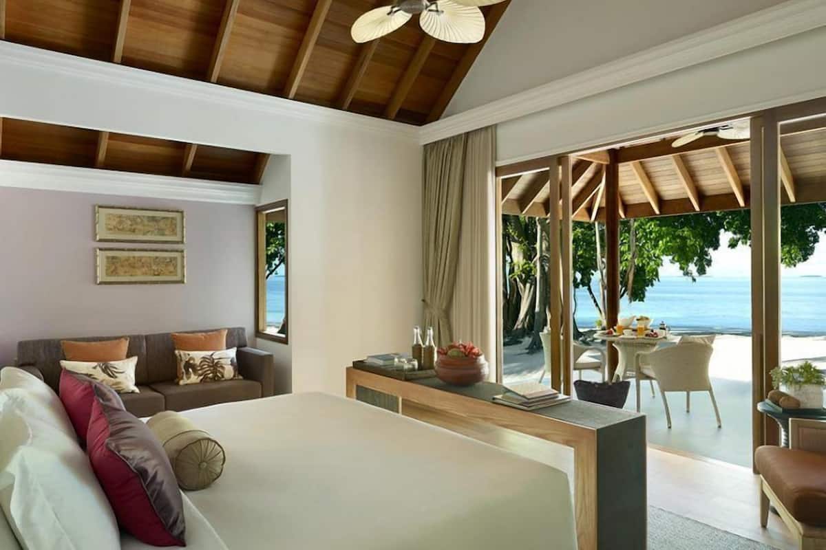 A bedroom with a large bed, a wooden desk, a sofa, and a view of the beach.