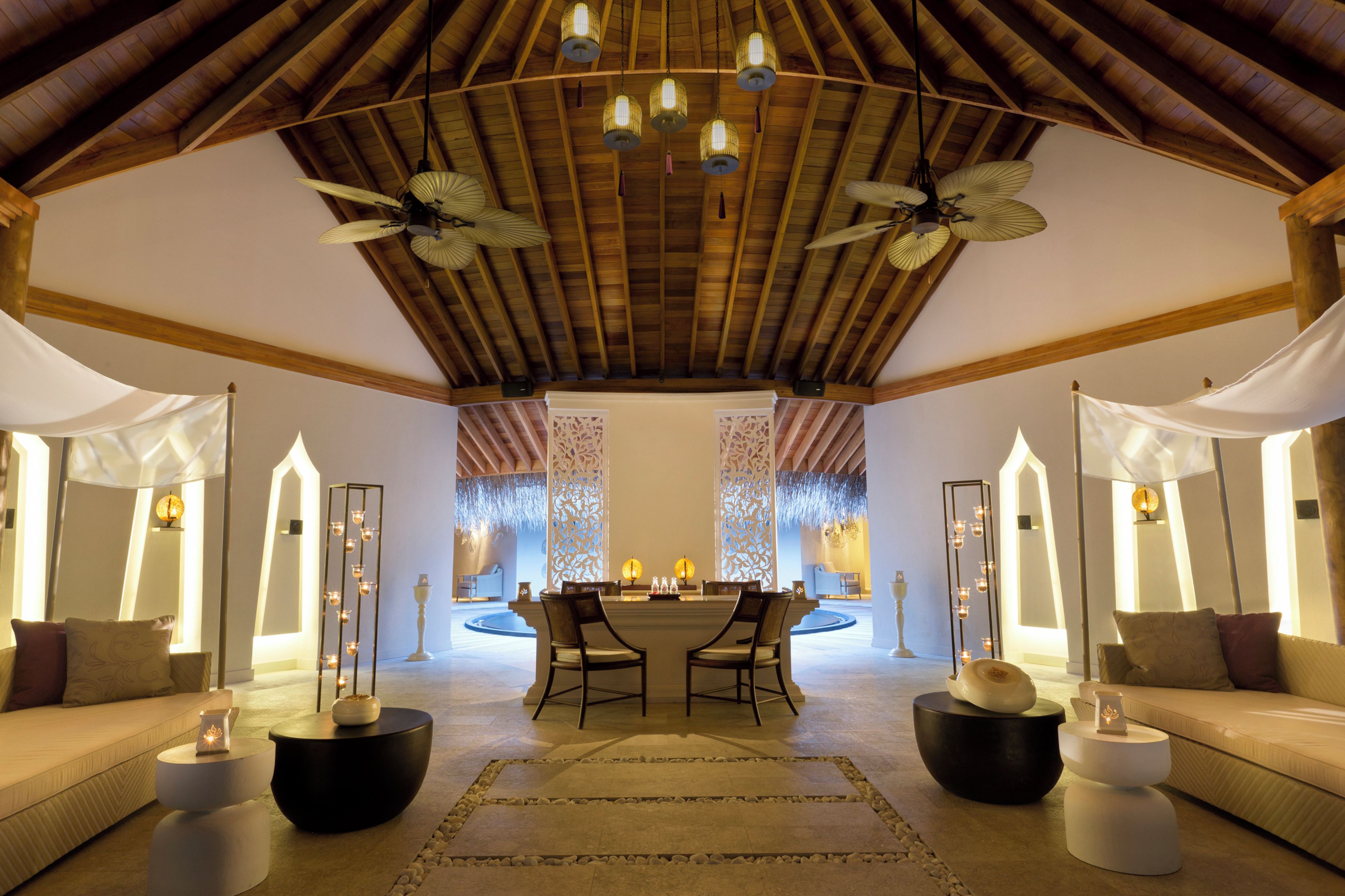 A spacious room with a high ceiling, wooden beams, and a central seating area with two chairs and a table.