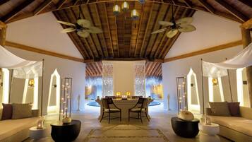 A spacious room with a high ceiling, wooden beams, and a central seating area with two chairs and a table.