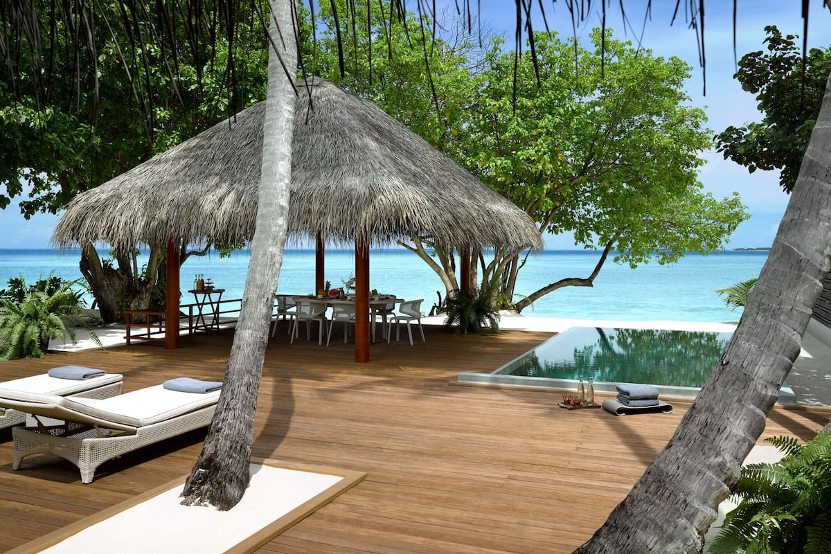 A wooden deck with lounge chairs, a thatched-roof structure, and an infinity pool overlooking the ocean.