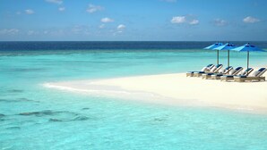 Una playa con aguas turquesas cristalinas, arena blanca y sombrillas azules que dan sombra a las tumbonas.