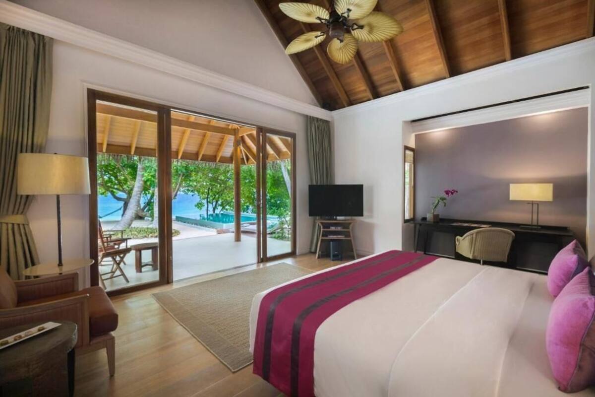 A hotel room with a bed, a TV, a desk, and a chair. There is a sliding glass door leading to a pool area.