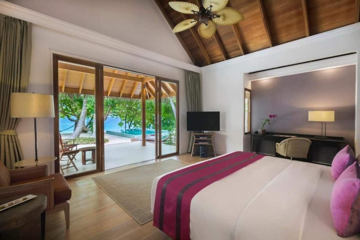 Habitación de hotel con cama, televisor, escritorio y silla. Hay una puerta corrediza de vidrio que da a una zona de piscina.