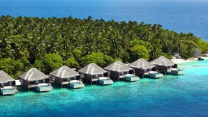 Overwater bungalows with thatched roofs and private pools, surrounded by a dense palm tree forest and the ocean.