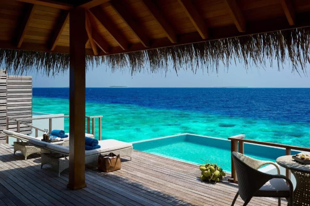 A wooden deck with lounge chairs, a small table, and a pool overlooking a clear blue sea.