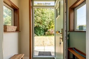 A wooden door with a sign reading 'MAYFIELD HOUSE' and a view of a garden with a bench and a window. - Kirkmay Road (No 18)  Mayfield House | Crail (Crail)