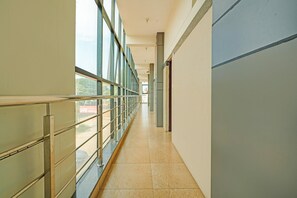 A corridor with a metal railing, large windows, and a tiled floor. - Hotel O Nanjundeshwara Temple (Nanjangud)