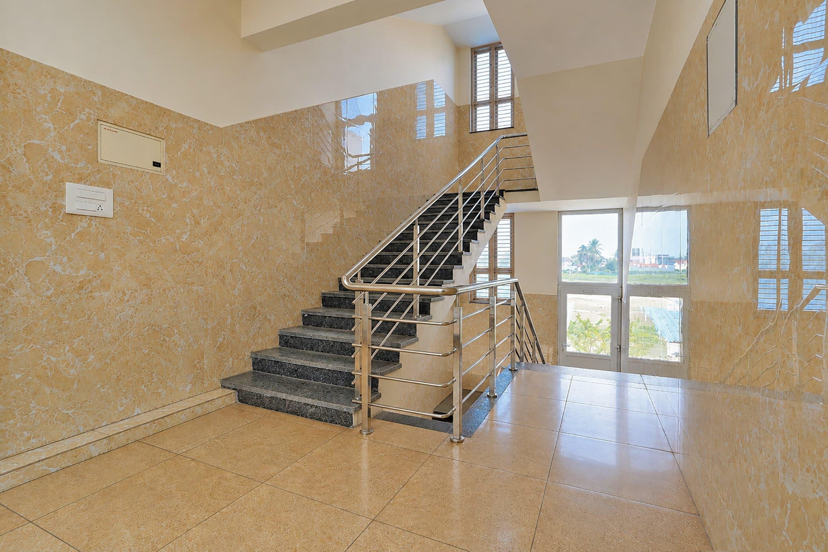 A spacious interior with a marble wall, a staircase with metal railings, and a large window providing a view of the outdoors.