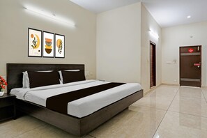 A hotel room with a large bed, a nightstand with a vase of flowers, and a door with a 'No Smoking' sign. - Hotel O Nanjundeshwara Temple (Nanjangud)