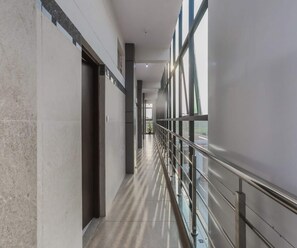 A corridor with a glass railing, a tiled floor, and a door on the left.