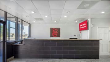A reception desk with a Red Roof Inn sign, a digital display advertising free Wi-Fi, and a view of the outside through large windows.