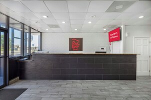 Un mostrador de recepción con el letrero de Red Roof Inn, una pantalla digital que anuncia Wi-Fi gratuito y vistas al exterior a través de amplias ventanas.