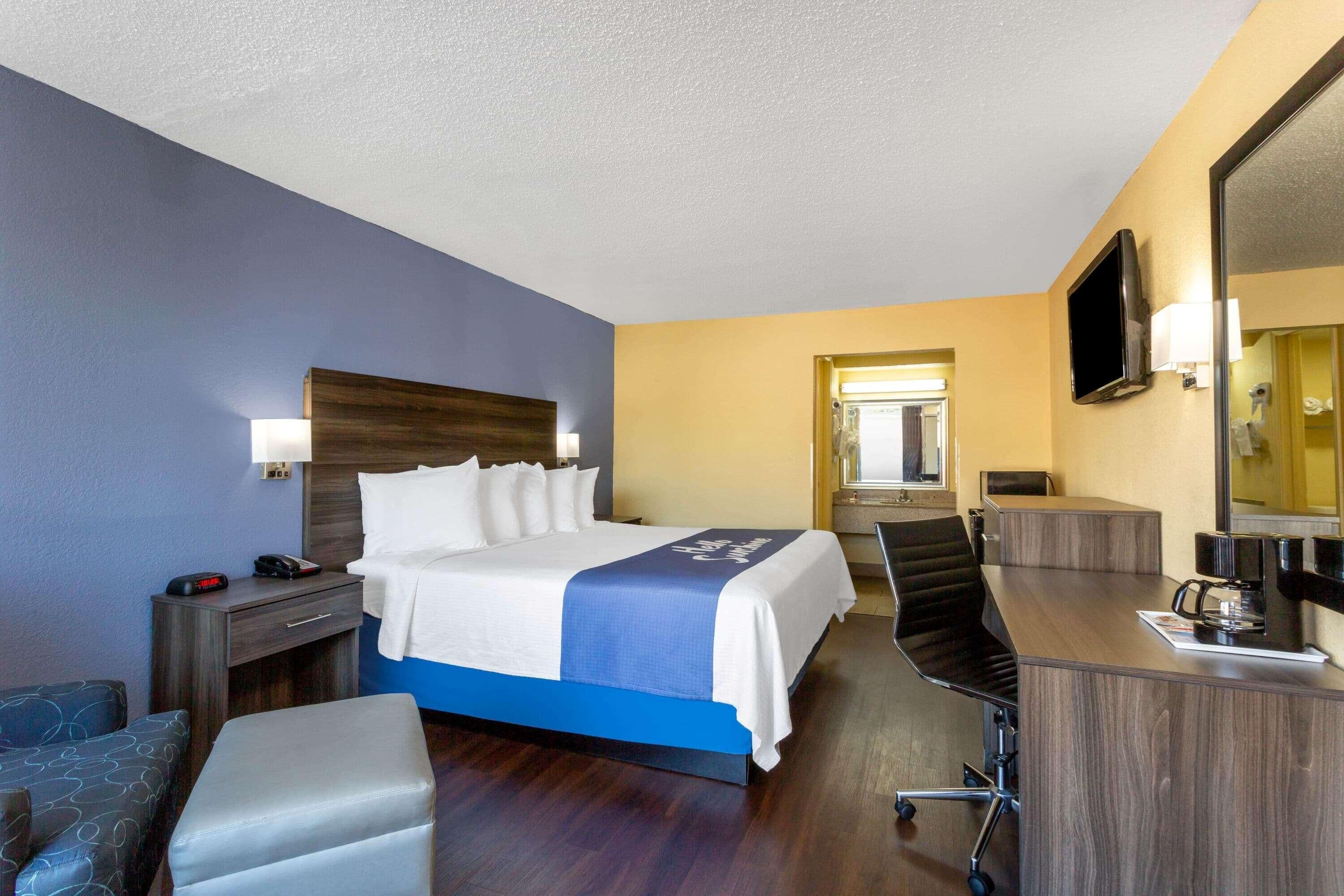 A hotel room with a bed, desk, chair, and a television.