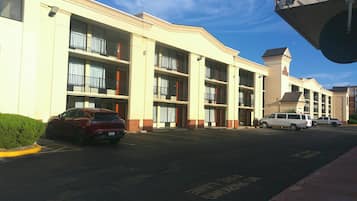 A multi-story hotel with balconies, a parking lot, and a clear sky.
