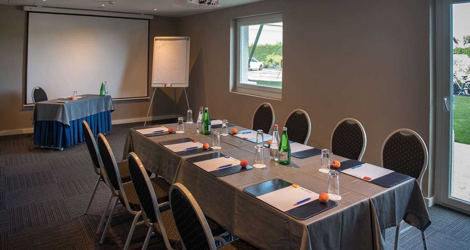 A conference room with a long table, chairs, a projector screen, and a whiteboard.