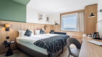 Une chambre d’hôtel avec un lit, un bureau, une chaise, une lampe et une fenêtre donnant sur un paysage agréable.