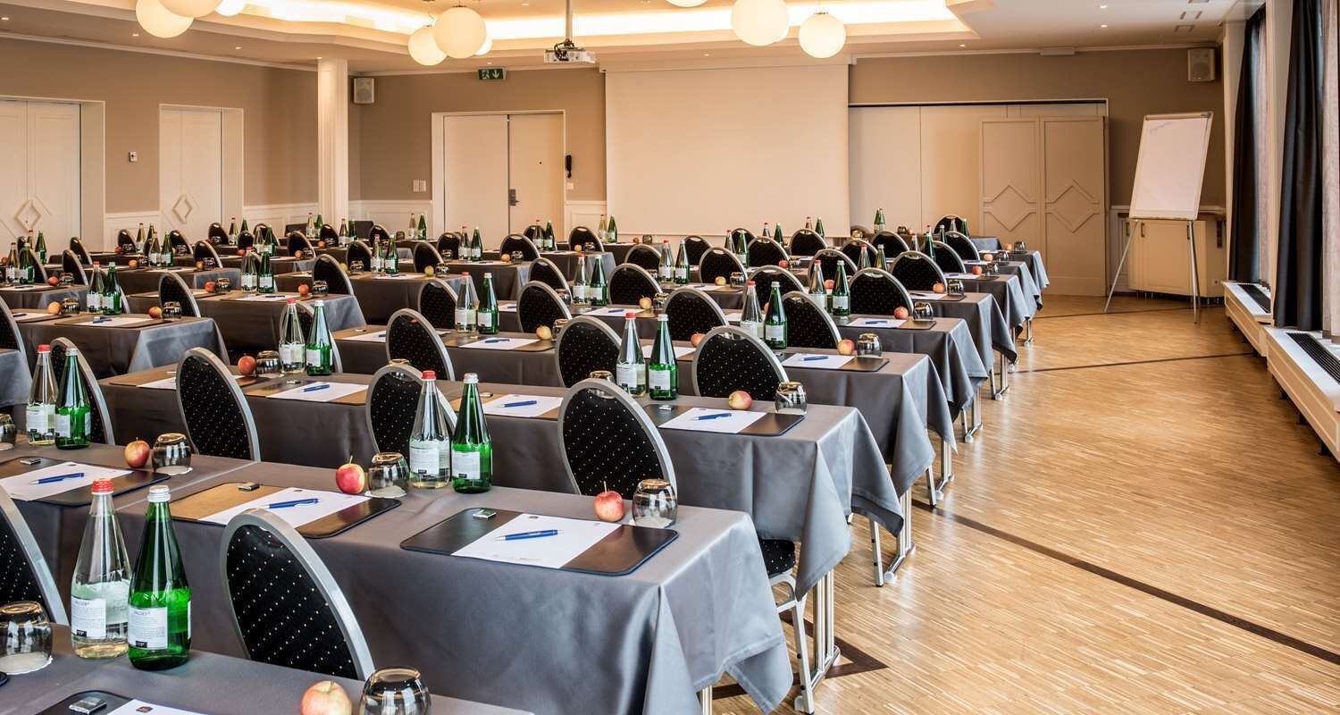 A conference room with rows of tables, chairs, and various items like bottles and apples.