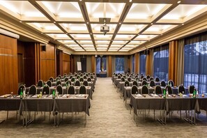 A conference room with rows of tables and chairs, a projector, and a large window with curtains.