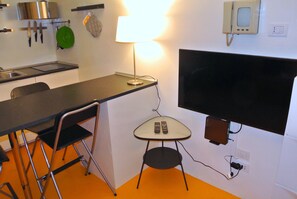 Eine kompakte Küche mit Essbereich, einem an der Wand befestigten Fernseher und einer Lampe auf einem kleinen Tisch.