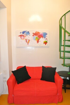 Ein rotes Sofa mit schwarzen Kissen, ein farbenfrohes abstraktes Gemälde an der Wand und eine grüne Wendeltreppe.