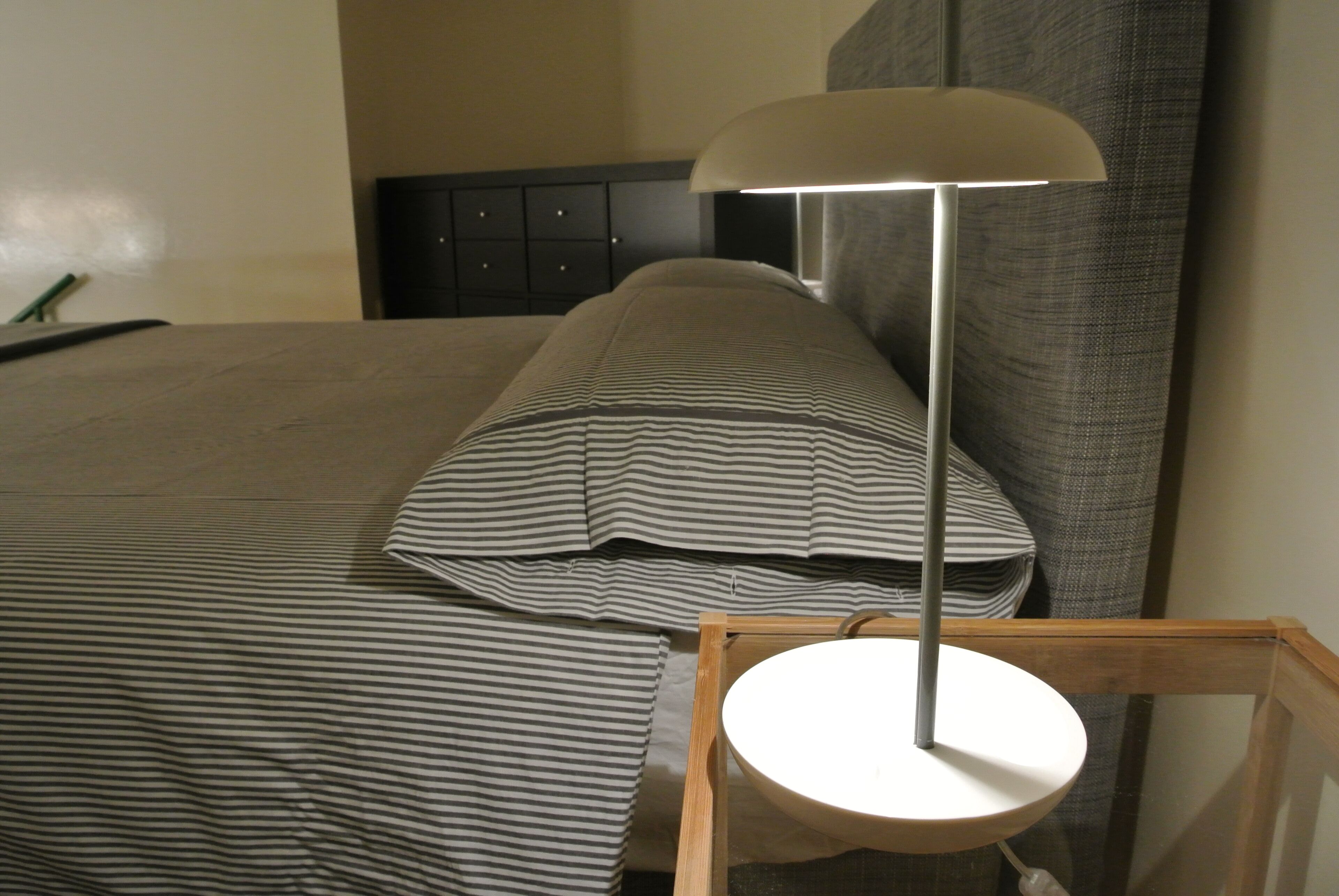 A neatly made bed with striped bedding, a bedside table with a lamp, and a dark headboard.