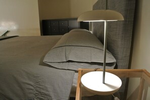 A neatly made bed with striped bedding, a bedside table with a lamp, and a dark headboard. - Vrbo Property (Milano)