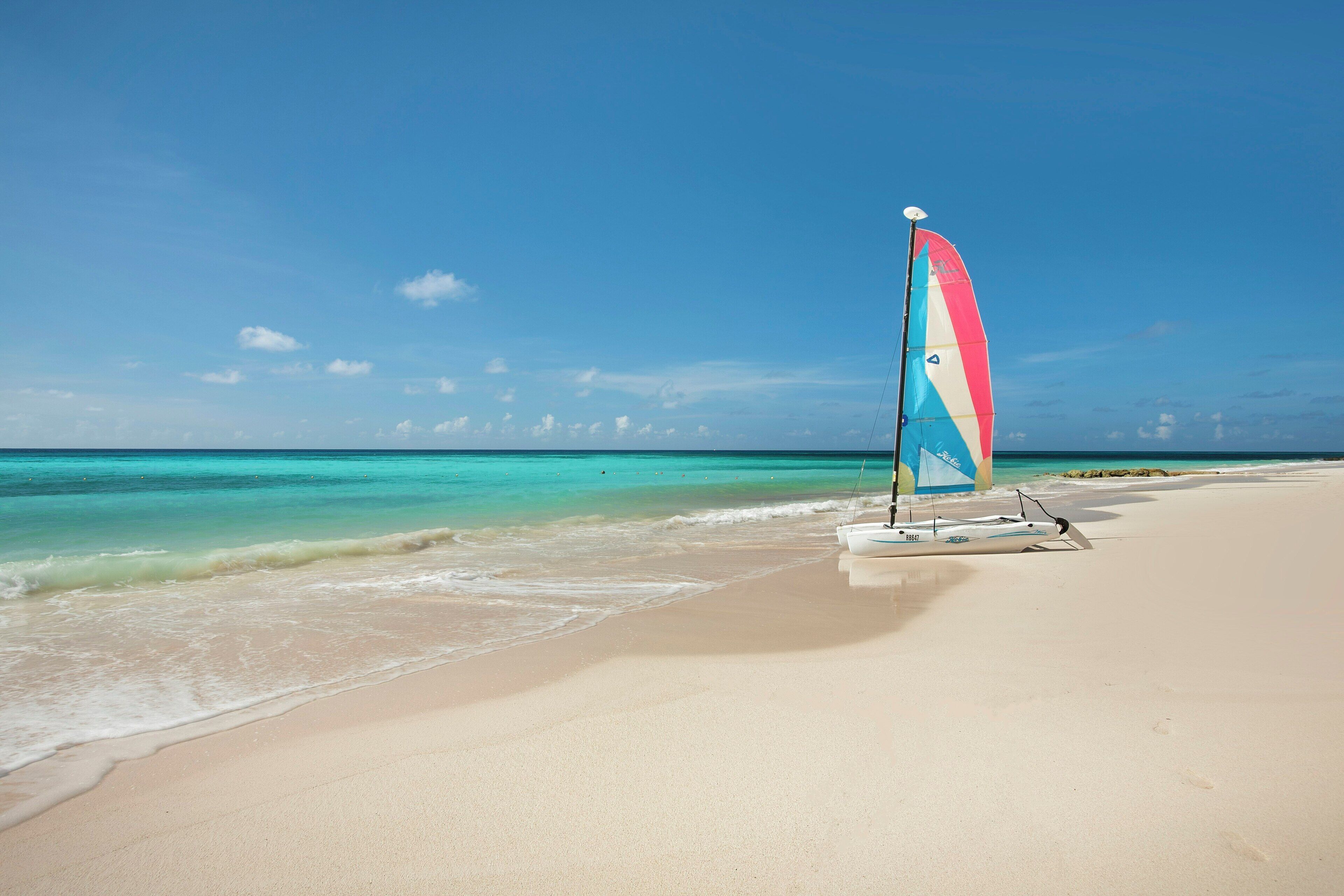 A beach with a sailboat and calm turquoise waters.
