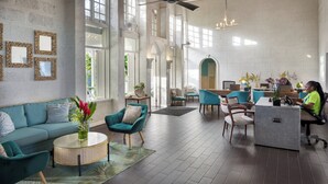 Eine großzügige Lobby mit hoher Decke, großen Fenstern und einer Sitzecke mit einer Couch und Sesseln.
