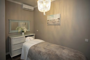 A bedroom with a bed, a dresser, a mirror, a chandelier, and a beach-themed painting. - Sea Breeze Beach House (Oistins)