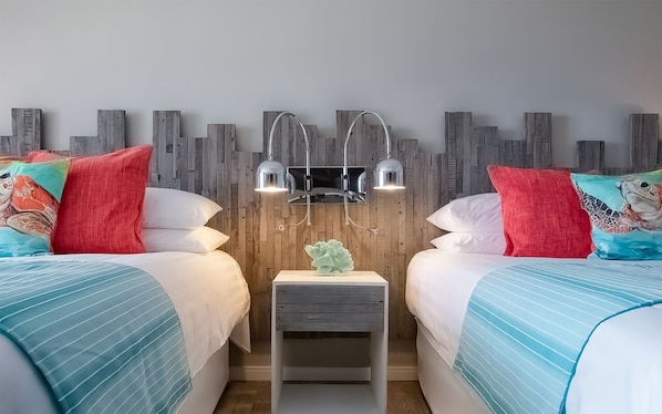 A hotel room with two beds, a nightstand with a lamp, and a wooden wall panel.