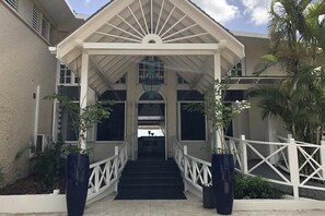 Una entrada cubierta con una escalera que conduce a un edificio, flanqueada por plantas en macetas y barandillas blancas.