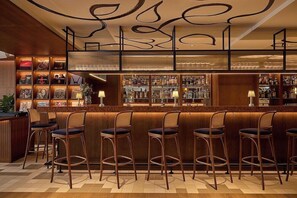 Un espace bar doté de nombreux tabourets et d’une étagère bien garnie de bouteilles d’alcool.