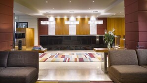A modern lobby with a flat-screen TV, sofas, a patterned rug, and a plant. - K+K Hotel Maria Theresia (Vienna)