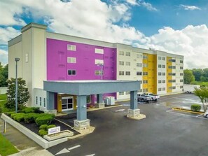 Et hotel med flere etager, med en facade i lilla og gul, en overdækket indgang og en parkeringsplads.