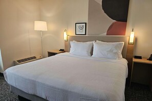 Habitació d'hotel amb un llit gran, dues taules de nit, una làmpada de peu i una obra d'art penjada a la paret.