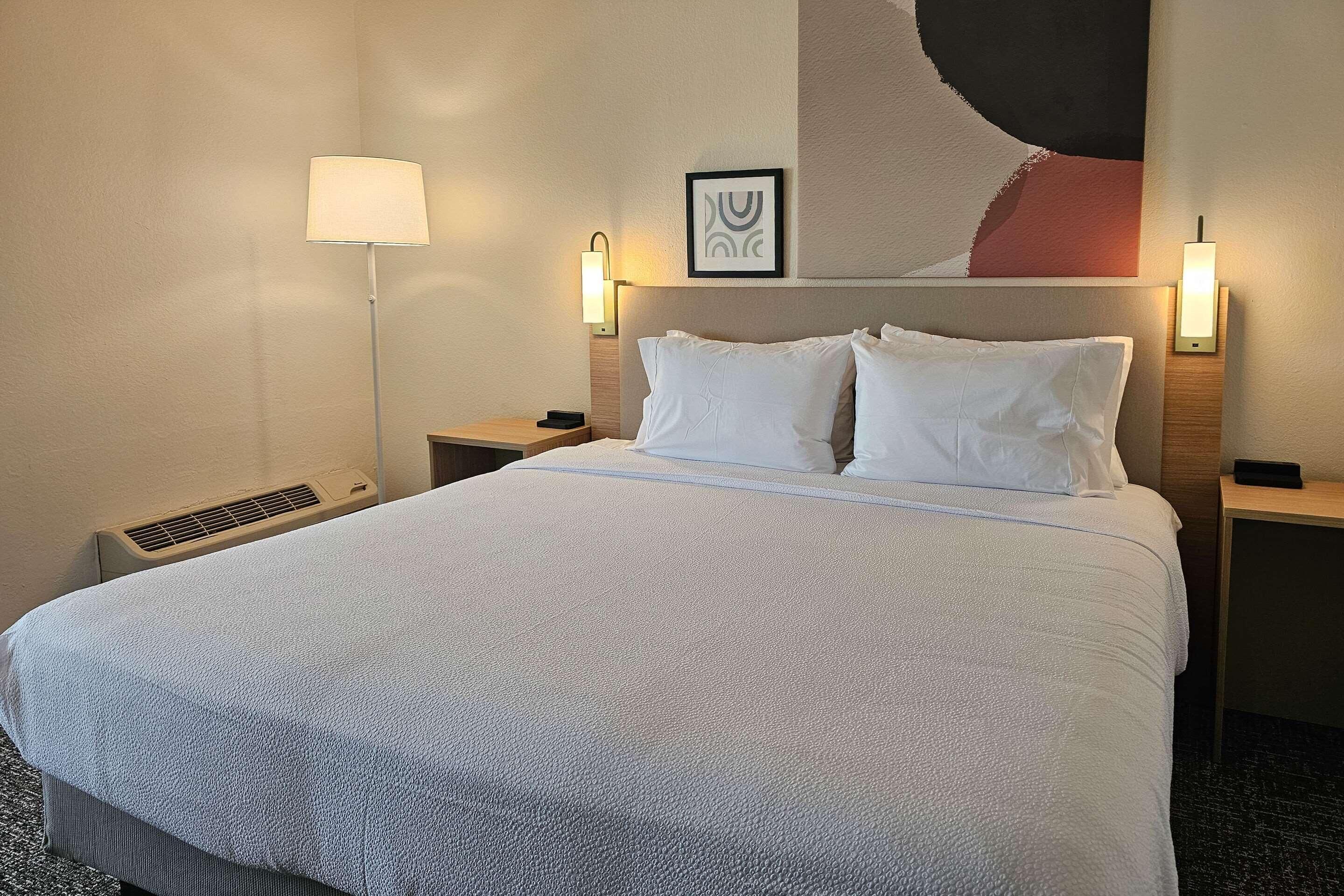 Een hotelkamer met een groot bed, twee nachtkastjes, een wandlamp en een lijst met een afbeelding.