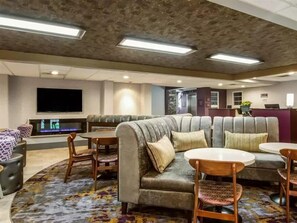Un hall d’hôtel comprenant un ensemble de canapés, un téléviseur à écran plat, un comptoir de réception et une moquette à motifs.