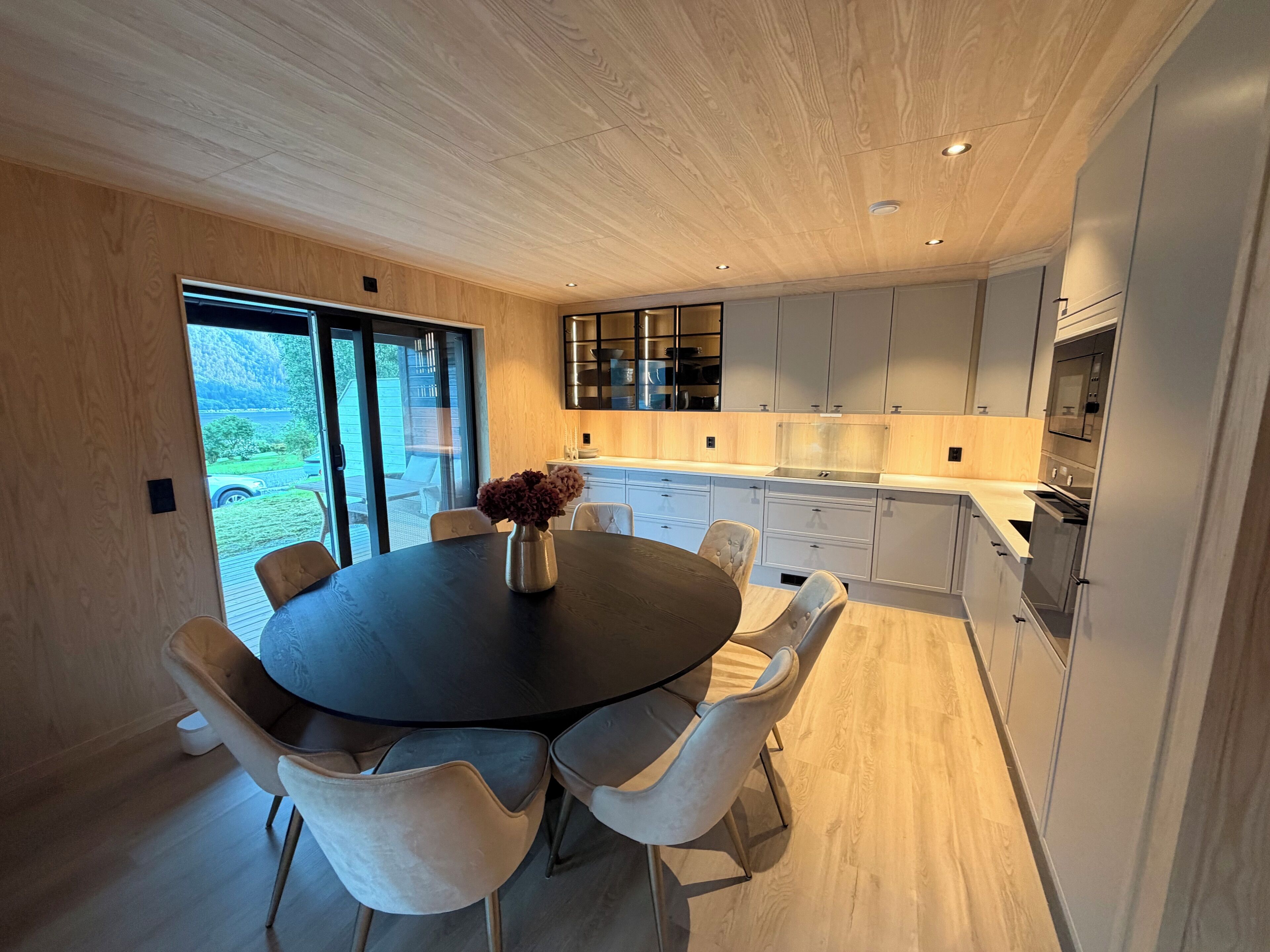 A modern kitchen with a round dining table, light wood cabinetry, and a view of the outdoors.
