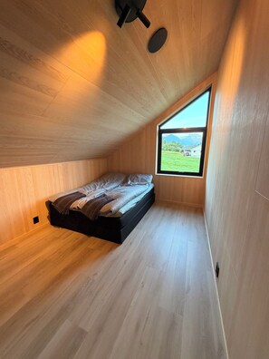 A room with a sloped ceiling, a bed, a window, and a view of a landscape.