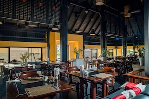 Un restaurante espacioso con techos altos, varias áreas de comedor y grandes ventanales con vistas.