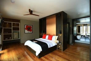 Quarto moderno com piso de madeira, cama com roupa de cama branca e vermelha, ventilador de teto e uma janela grande.
