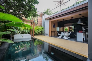 Uma área moderna para refeições ao ar livre com piscina, deck de madeira e vista para a cozinha.