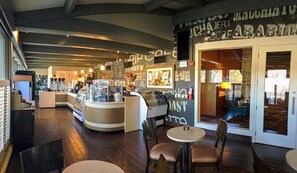 L’intérieur d’un café, avec un comptoir, un espace salon et une vue sur l’extérieur.