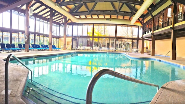 Una piscina interior con agua cristalina, rodeada de sillones de descanso y una zona de estar techada con ventanales grandes.