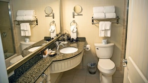 Un baño con dos lavamanos, un inodoro, un espejo y toalleros.