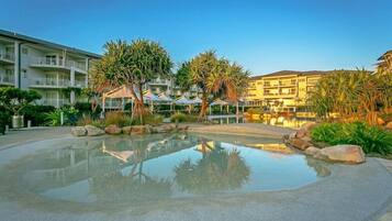 A hotel with a swimming pool, palm trees, and a clear sky.