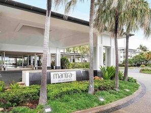 Entrada moderna de un hotel con un paseo techado, palmeras y un letrero que dice 'mantra on salt beach'.