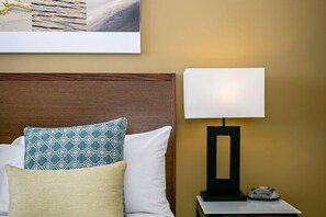 Una habitación de hotel con una cama bien hecha, una mesita de noche con una lámpara y un cuadro enmarcado sobre la cama.