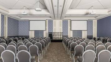 A conference room with rows of chairs, a stage, and two large screens.