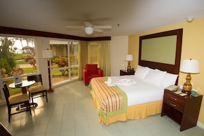 A hotel room with a bed, a chair, a table, a nightstand, and a view of the outdoors.